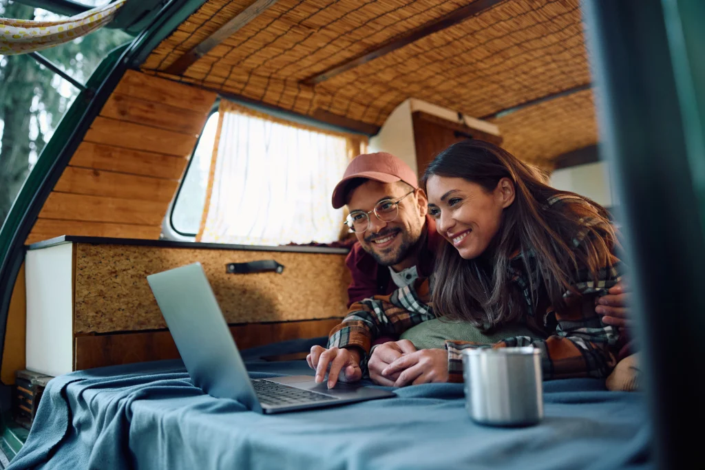 happy-couple-of-campers-surfing-the-net-on-laptop-on-their-van-in-the-woods
