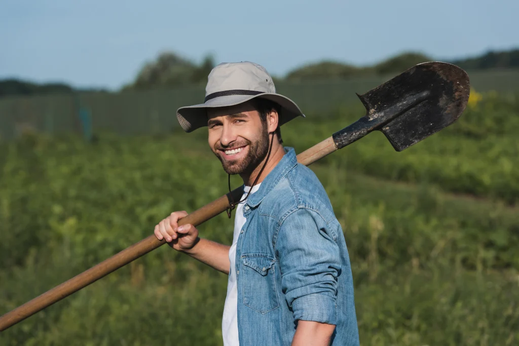 farmer-in-brim-hat-smiling-at-camera-while-holding-shovel