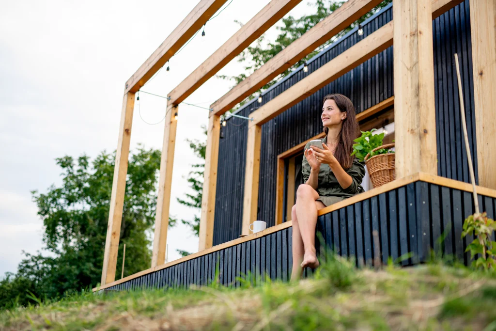 young-woman-with-smartphone-outdoors-weekend-away-in-container-house-in-countryside