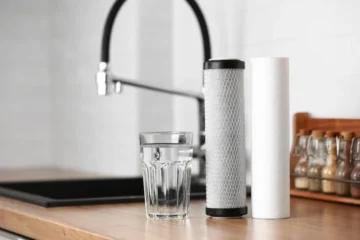 Kitchen faucet beside a glass of water and replacement water filter cartridges