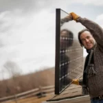 Man carrying a solar panel onto a roof for an off-grid backup system