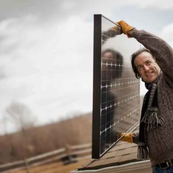 Man carrying a solar panel onto a roof for an off-grid backup system